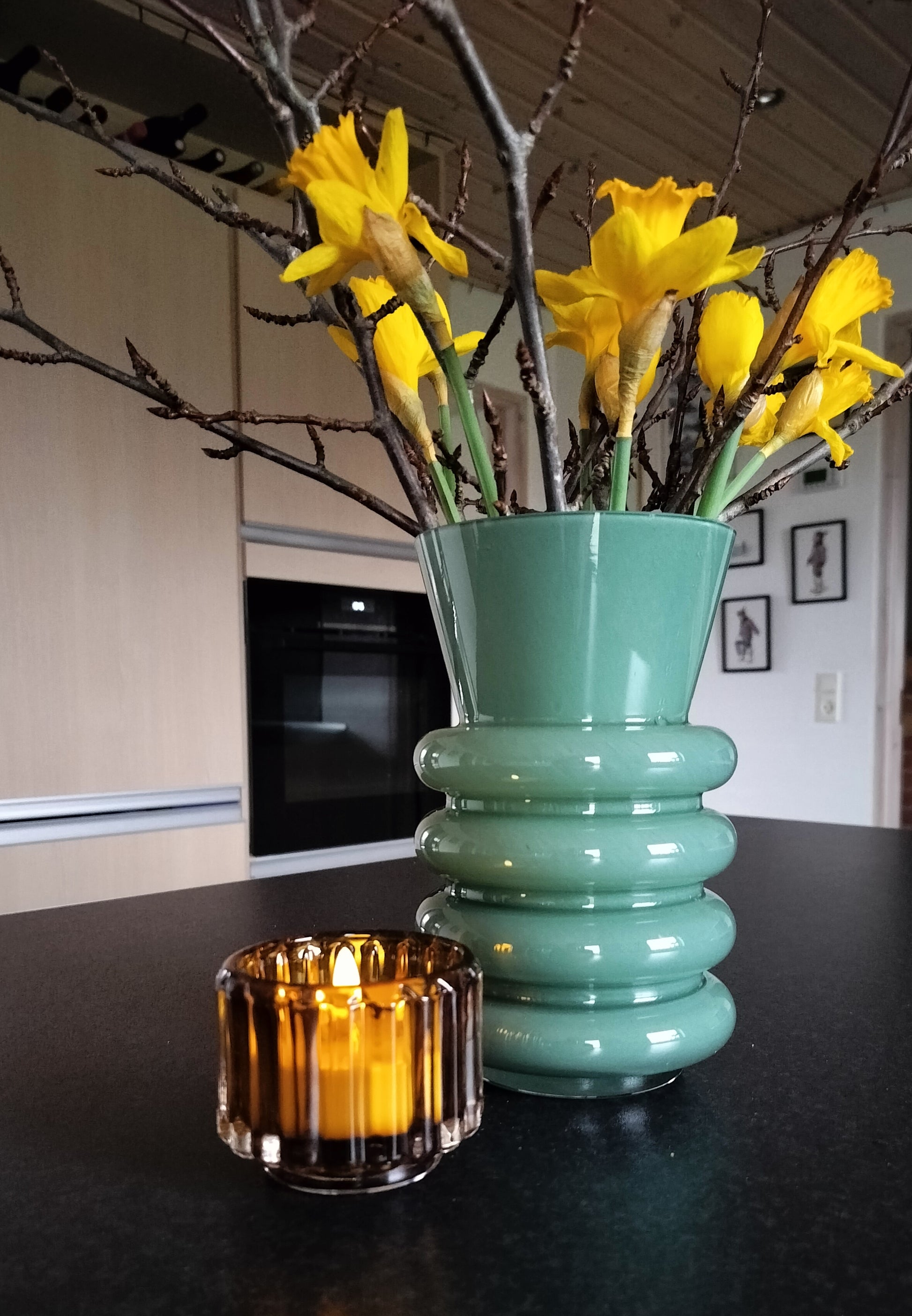 Fyrfadsstage i rav farve foran mintgrøn vase.
